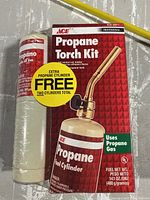 Photo of sealed propane torch kit in box with attached propane cylinder and extra propane cylinder wrapped in plastic beside it. Box states propane torch kit uses propane gas and has extra propane cylinder free, two total cylinders.