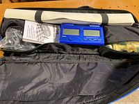 Top view inside the black soft carrying case showing rolled-up vinyl chess board, Saitek digital chess timer, chess pieces in plastic bags, and manual.