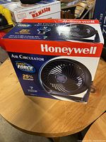 Full box view showing Honeywell Air Circulator fan in packaging on wooden table.