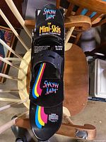 Top view of one black Snow Jam toy mini-ski with multicolor stripes and built-in adjustable bindings, showing branding and usage text.