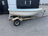 Side view of small fiberglass sailboat on trailer, showing hull and trailer frame