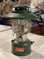 Front view of vintage Coleman lantern showing green metal base and domed top with glass globe and mantles inside.