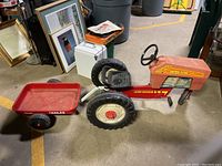 Side view of red vintage AMF Turbo Trac pedal toy tractor number 437 with Sears tow trailer attached, showing treaded rear wheels, pedals, steering wheel, seat, and trailer labeling.