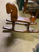 Side view of vintage wooden rocking horse showing the curved seat, head with handles, and rockers under the horse body.
