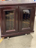 Front view of dark wood cabinet with two glass paneled doors on wheels.
