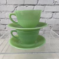 Two stacked pale green jadeite tea cups with matching saucers showing ribbed texture and handle detail.