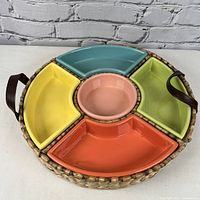 Top view of the round, colorful ceramic segmented serving dish assembled on a woven wicker tray with leather handles.