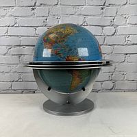Front view of globe in atomic metal cradle stand against white brick background.