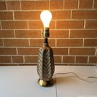 Full view of the vintage ceramic bedside table lamp base lit up with a bulb, showing shape and style