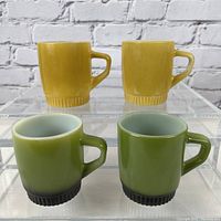 Front side view of two yellow and two green Fire King coffee mugs showing their ribbed base and handle design.