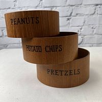Three wooden bowls nested and stacked, clearly showing the labels 'PEANUTS', 'POTATO CHIPS', and 'PRETZELS'.