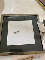 Full view of framed matted abstract art with two black ink circular designs and dotted curved lines on white background.
