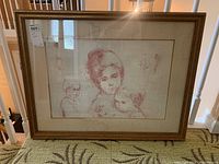 Frontal view of the signed lithograph depicting a woman and two children in red tones, framed in a gold frame with visible water damage.