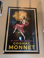Full-view of framed Cognac Monnet poster hung on wall showing central figure and text