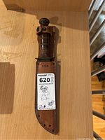 US Navy knife in leather sheath lying on wooden surface, showing leather handle top and sheath front.