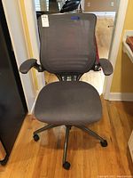 Full front view of gray desk chair showing mesh back, cushioned seat with some stains, armrests, and caster wheels.