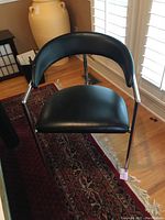 Front close-up of a black seat and back chair with a chrome metal frame showing curved backrest and padded seat
