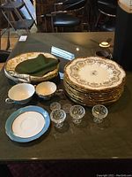 Overview of stacked dinner plates, teacups, salts and containers on green table