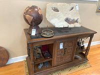 Wide view showing wooden globe, West London compass, animal figurines, wine stopper case, stone fossil on stand, all on wood cabinet.