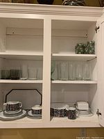 Cabinet shelves with Rosenthal china set on lower shelves and green floral juice glasses plus clear glasses on upper shelves.