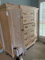 Front and side view of dresser showing six center drawers with black metal pulls and open left cabinet door with round wooden knob.