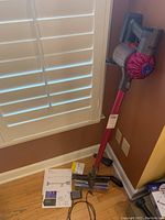Dyson V6 vacuum mounted on wall with stick and accessories near wall outlet