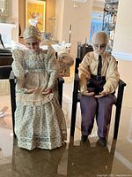 Front view of the elderly couple figurines seated in chairs showing detailed facial features, clothing textures, and colors.