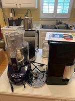 Photo of kitchen counter with Starbucks Barista cappuccino maker, Cuisinart Mini Prep Plus food processor, Mini Mate Plus grinder, and Prep 11+ food processor along with accessories and cords visible.
