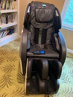 Full front view of brown massage chair showing seat, armrests, and foot massager compartments