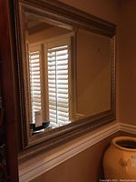 Full frontal photo of large mirror reflecting dining room with white shutters, showing the beveled edge and decorative metallic frame.
