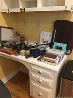 Desk with office supplies scattered, including lamp, mouse, pen holders, staplers and documents.