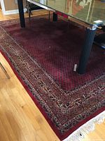 Full view of red rug under glass-top table, showing overall dimensions and pattern.
