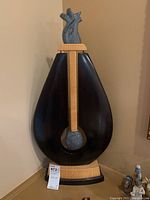 Front view of sculpture showing large teardrop dark wood frame, light wood vertical support, and swinging stone in center.