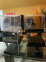 Six clear acrylic sports memorabilia display cases stacked in two columns on a glass table, showing the transparent case and black base.