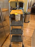 Front view of the Cosco step ladder with black steps and yellow top, showing paint splatters on steps.