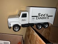 White metal See's Candies truck model with black wheels and clear logo lettering.