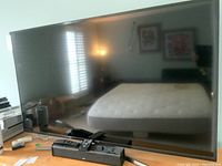 Front view of Samsung TV on stand with Zvox speaker and two remotes on wooden dresser