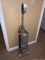 Front view of the upright vacuum showing handle, dust container, hose attached to side and cleaner head on carpet.