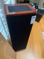 Full height front view of speaker with black grille and cherry wood top panel