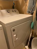 White Whirlpool electric dryer with front-loading door, lint trap on top, situated in laundry room.