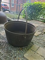 Front view angle of large cast iron cauldron with bail handle on gravel and paver surface