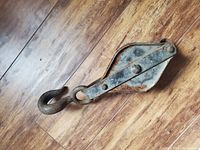 Photo of an antique metal pulley with a hook placed on a wooden floor, showing rust and wear on the metal surface.