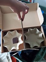 Two cream-colored Pampered Chef stoneware baking dishes with scalloped edges side by side in an open cardboard box showing size and shape.