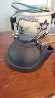 Front and side view of black cast iron kettle showing coil spring handle and spout.