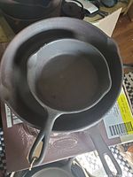 Photo showing two round cast iron pans stacked, smaller pan inside larger pan, both cleaned and seasoned with single handles visible.
