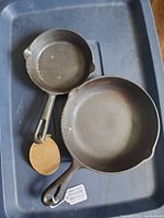 Two cast iron frying pans placed in a container, showing top and interior surfaces with some residue and wear.