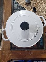 Top view of white enameled Cuisinart Dutch oven lid with black knob, showing some surface wear.