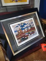 Overall view of the framed signed print, showing the silver and black frame and colorful landscape artwork.