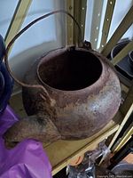 Photo of a rusted large cast iron kettle showing front and side view with handle and spout.