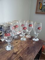 Seven Stella Artois beer glasses displayed on table, all with clear glass and gold rim.